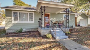 A single-story house with a front porch, a small garden area, and a visible garage. - Missouri Escape w/ Furnished Patio, Near Downtown! (Nevada)