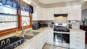 A kitchen with white cabinets, a stainless steel sink, a microwave, a stove, and a window with a blue valance. - Missouri Escape w/ Furnished Patio, Near Downtown! (Nevada)