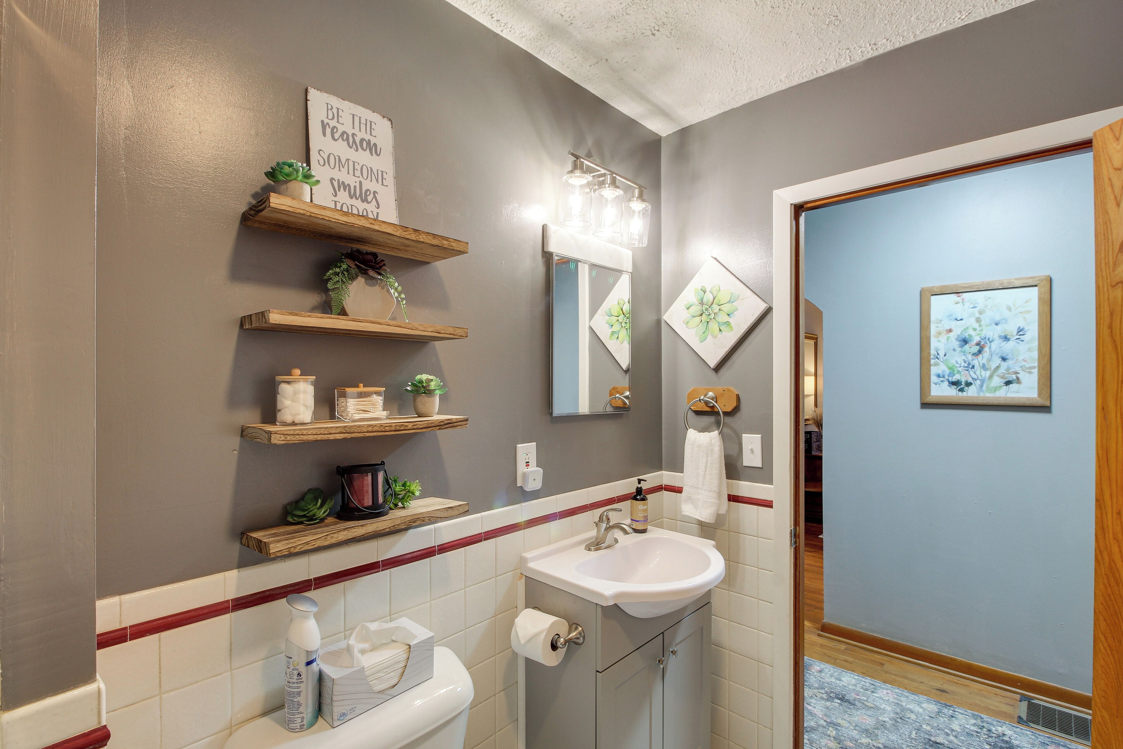 A bathroom with a toilet, sink, and shelves with toiletries. There is a mirror above the sink and a sign on the wall.