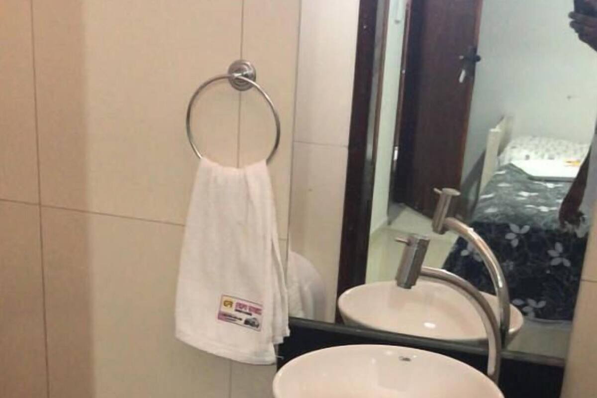 Un baño con un lavamanos blanco, un espejo y una toalla colgada en un aro metálico.
