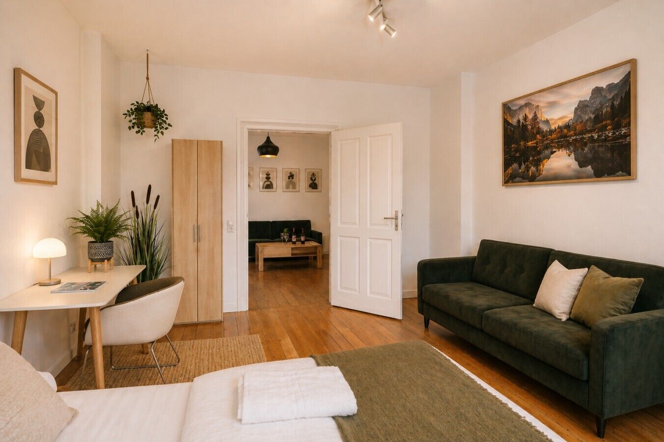 Een moderne woonkamer met een groene bank, een houten salontafel, een wit bureau met een lamp en een schilderij aan de muur.