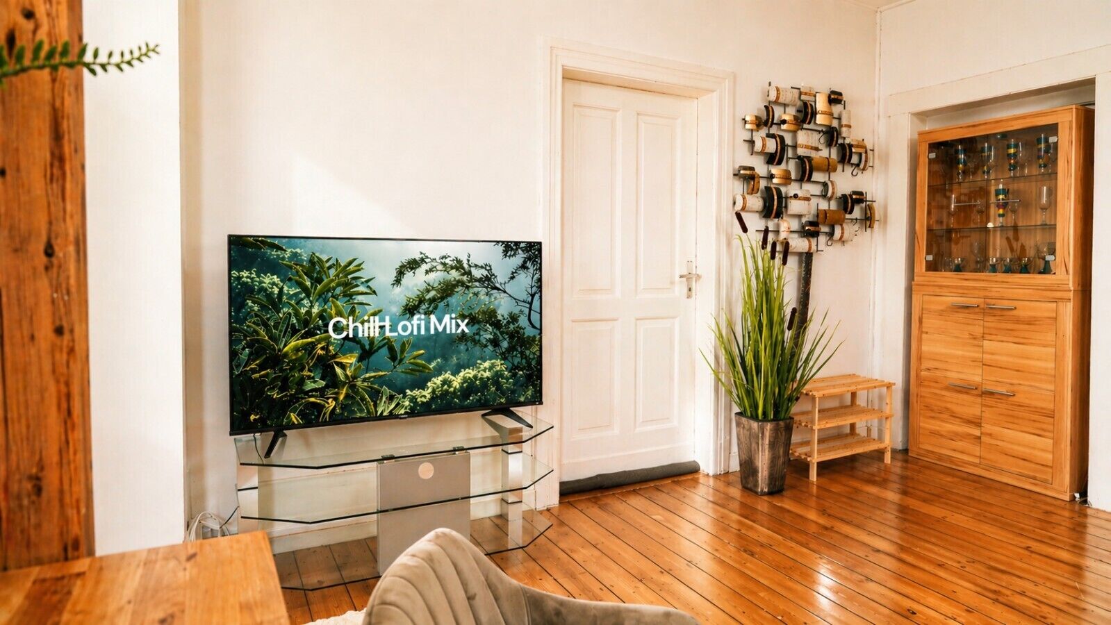 A living room with a flat-screen TV, wooden flooring, a potted plant, and a cabinet with glass doors.