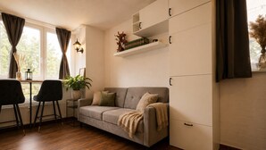 A modern living room with a sofa, a dining table, chairs, a potted plant, and built-in cabinets. - Stylish & Quiet Studio | Parking | WIFI | TV (Bielefeld)