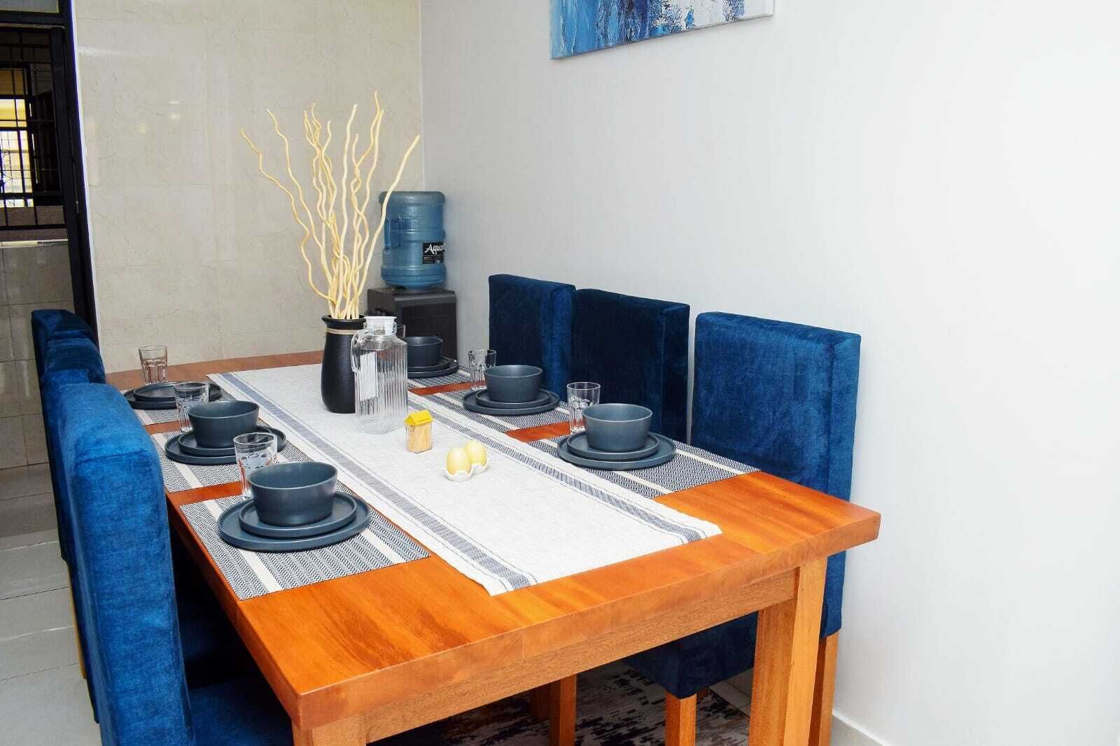 Une table à manger dressée avec de l’assiette, des bols et des verres noirs, entourée de chaises à revêtement bleu.