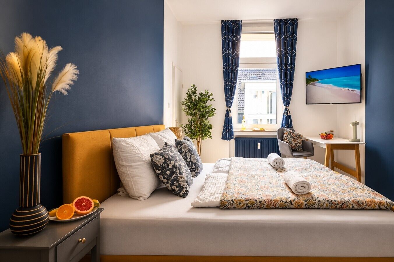 Ein Hotelzimmer mit Bett, Schreibtisch, Stuhl, Fernseher und einem Fenster mit Vorhängen.