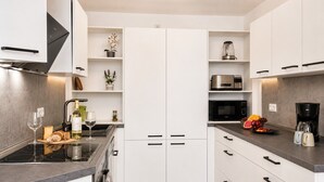 Eine moderne Küche mit weißen Schränken, einer eingebauten Mikrowelle, einer Kaffeemaschine und einer Obstschale.