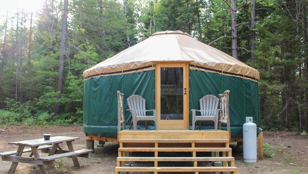 Puinen kuisti ja kaksi Adirondack-tuolia ympäröivät jurttaa, ja kaiken tämän ympärillä on metsä.