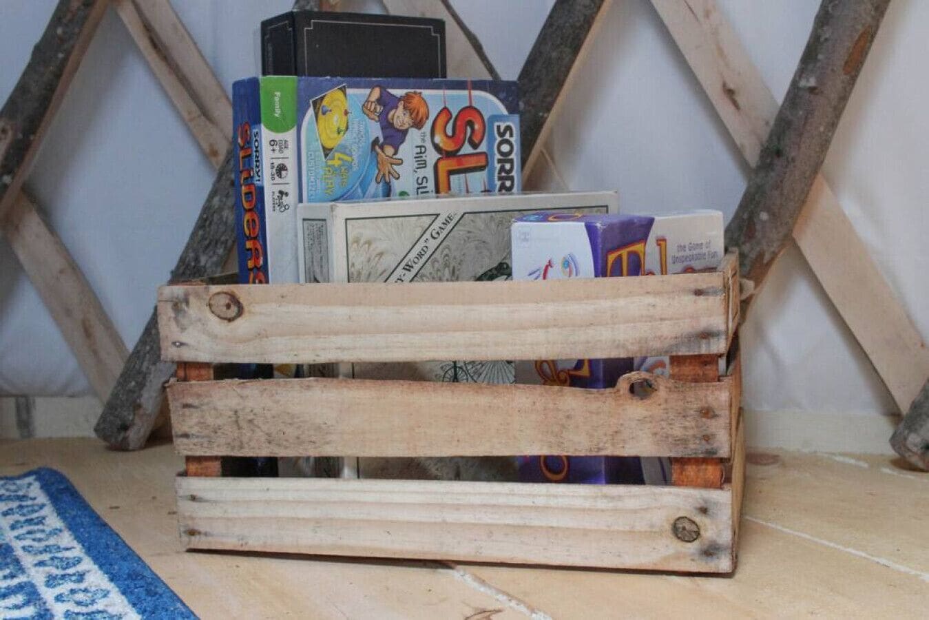 A wooden crate filled with books and magazines, placed on a tiled floor with a blue rug.
