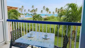 A balcony with a table and chairs, overlooking a pool and palm trees.