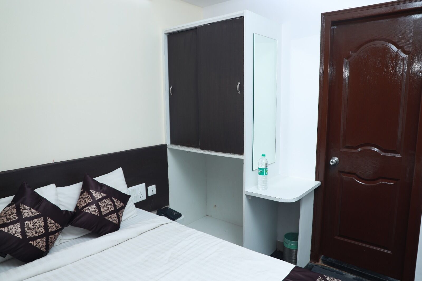 Un dormitorio con cama, armario, espejo, botella de agua y una puerta.