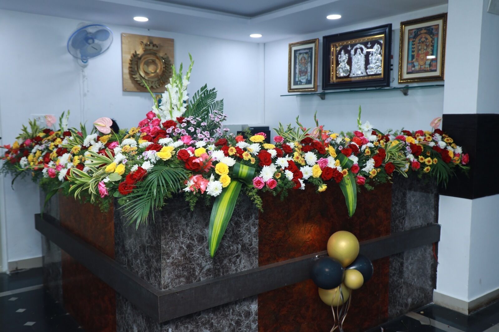 En receptionsdisk med blomsterarrangement, indrammede billeder og en ventilator.