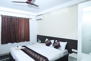 A hotel room with a bed, a ceiling fan, an air conditioning unit, and a bedside table with a bottle of water. - Urban Stay Chairmen Hotel (Bengaluru)