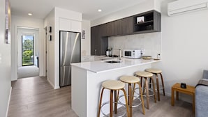 Une cuisine moderne dotée d’un îlot central, de tabourets de bar, d’un réfrigérateur, d’un four à micro-ondes et d’une cuisinière.