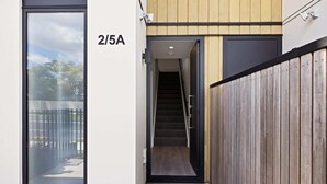 Une entrée moderne avec une façade en bois, une porte en verre et un escalier menant à l’intérieur du bâtiment.