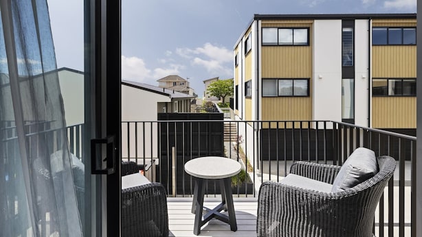 Un balcon agrémenté de meubles en osier, une petite table ronde et une vue sur les immeubles voisins.
