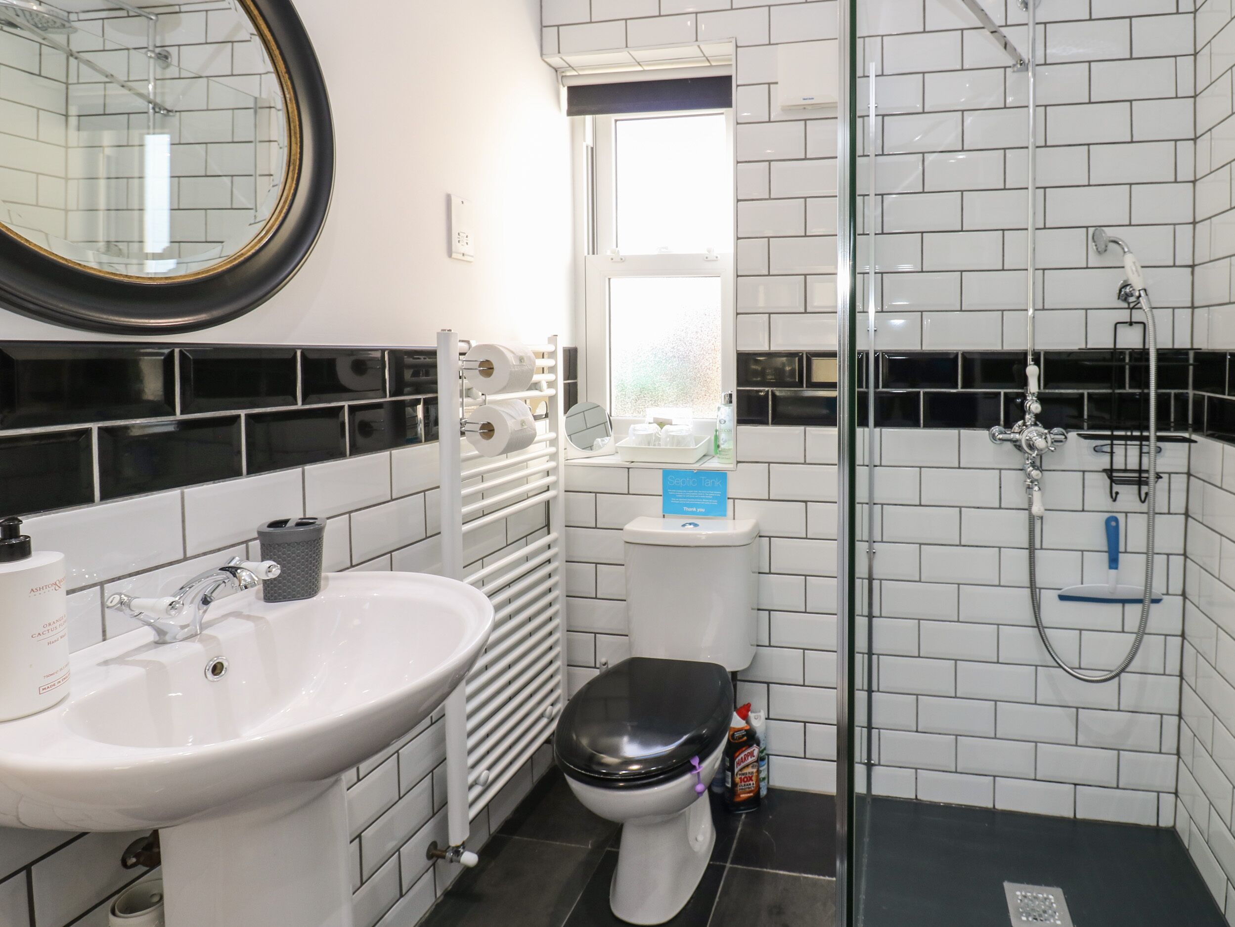 Un baño moderno con lavamanos blanco, inodoro negro y zona de ducha con mampara de vidrio.