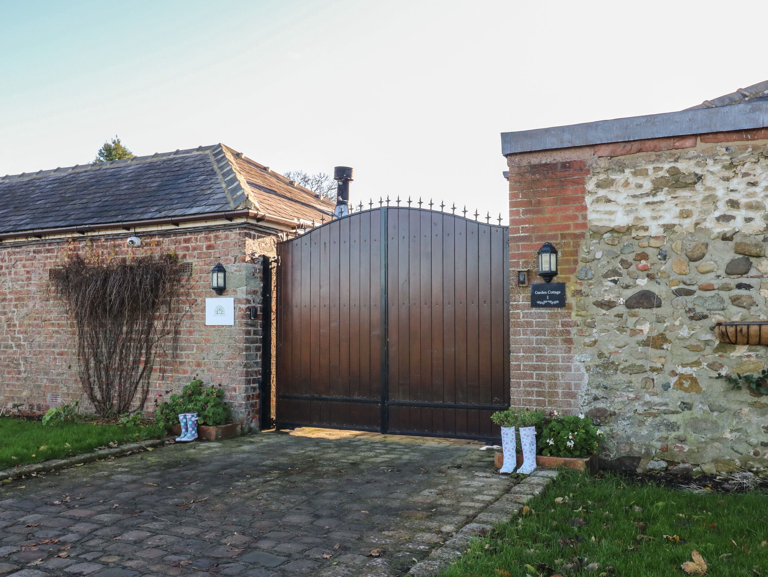 A brick building with a large wooden gate, a stone wall, and a sign that reads "Garden Cottage."