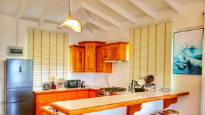 A kitchen with wooden cabinets, a stainless steel refrigerator, a large island with stools, and a hanging light fixture. - Blue Whale Villa - Penthouse (Calibishie)