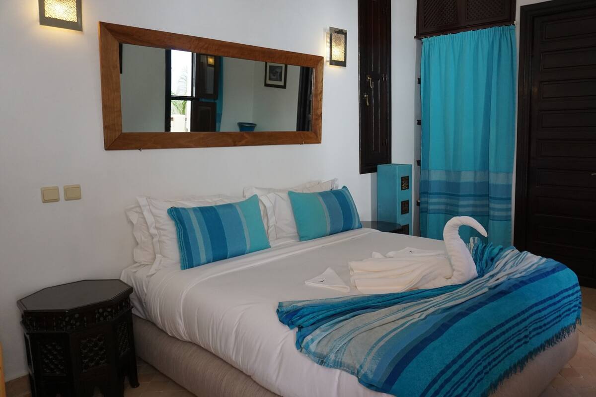 A bedroom with a bed, a mirror, a door, and a small cabinet.