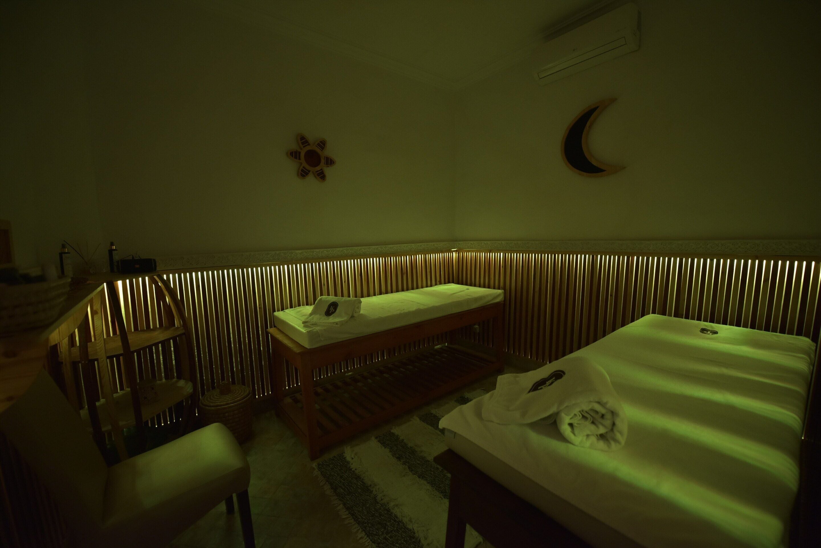A room with a bed, a bedside table, a chair, a small table, and a wall-mounted shelf.