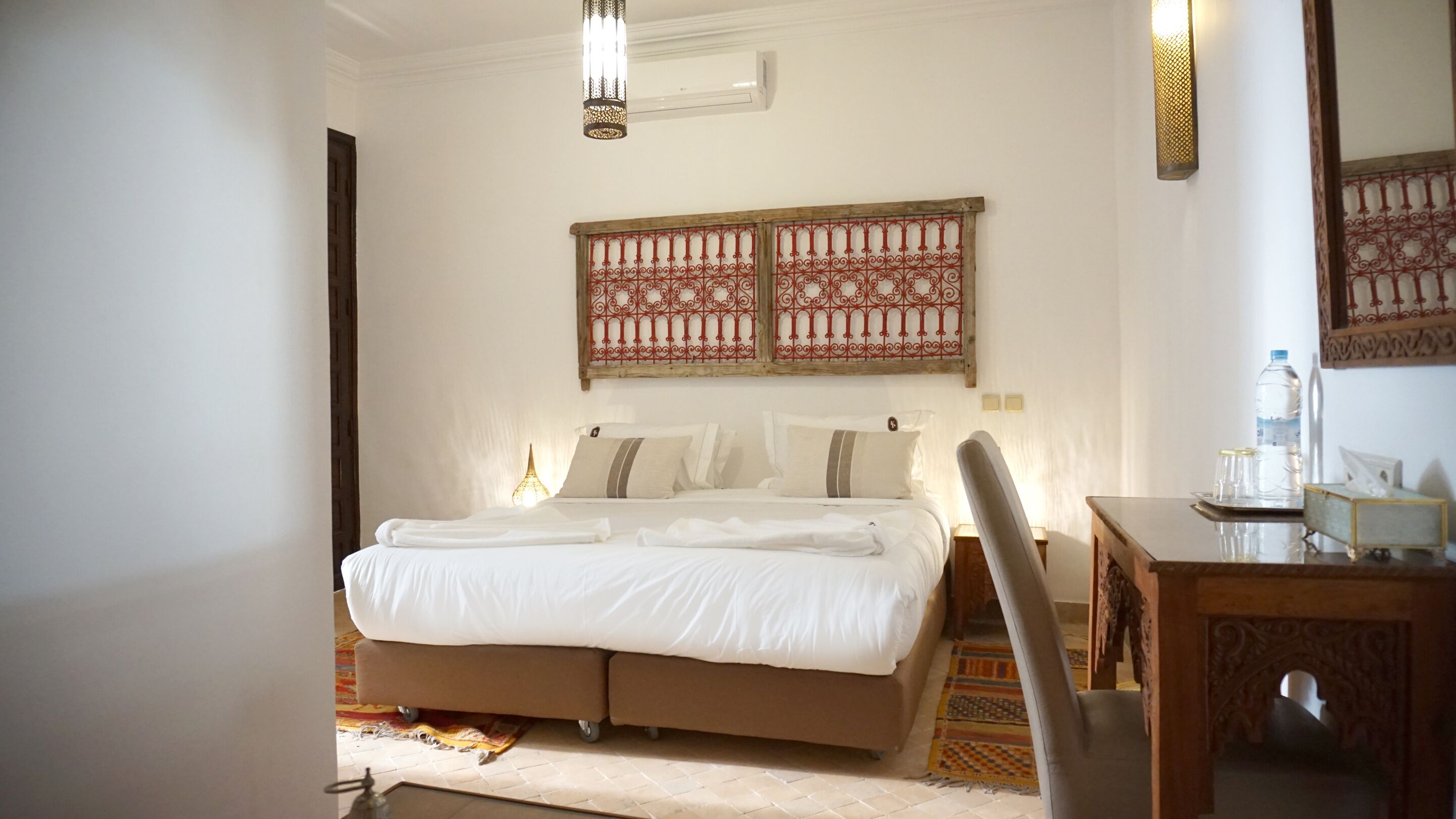 A bedroom with a bed, bedside tables, a chair, a desk, and decorative wall panels.