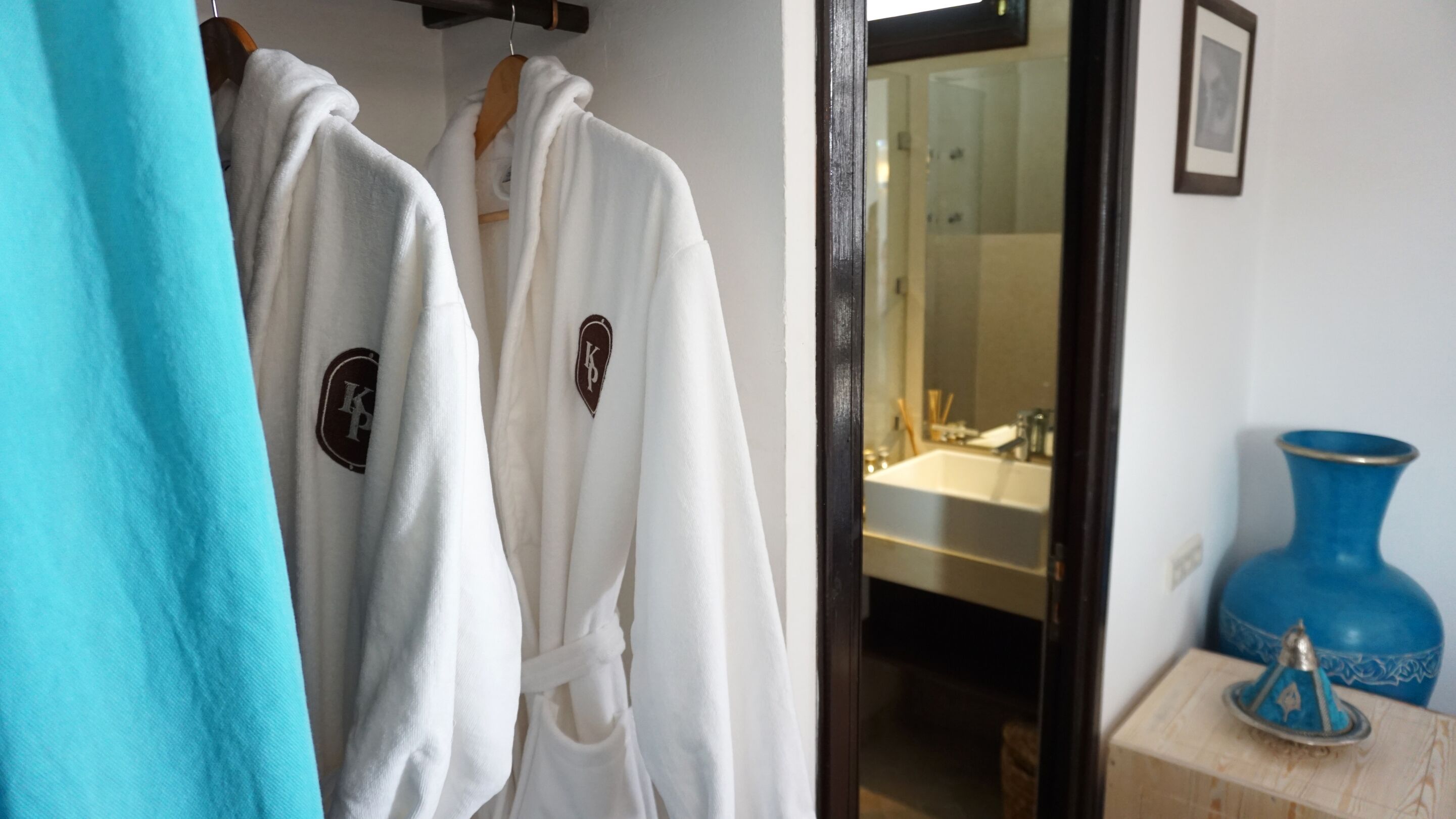 Un baño de hotel con un lavabo, un espejo y un jarrón azul sobre una mesa de madera.