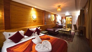 Une chambre d’hôtel avec un mur en bois, un lit recouvert d’une couverture rouge et orange, une serviette en forme de cygne et un fauteuil en cuir.