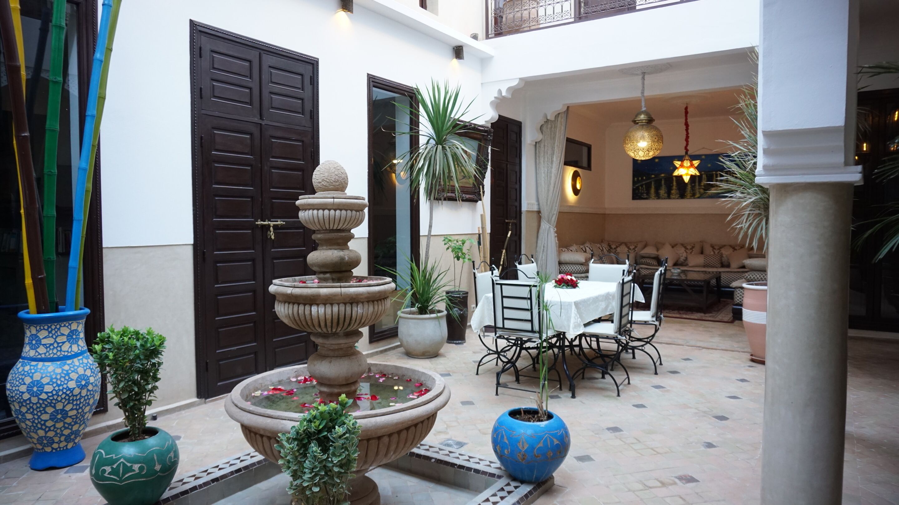 A courtyard with a fountain, potted plants, a dining area with outdoor seating, and a large door.