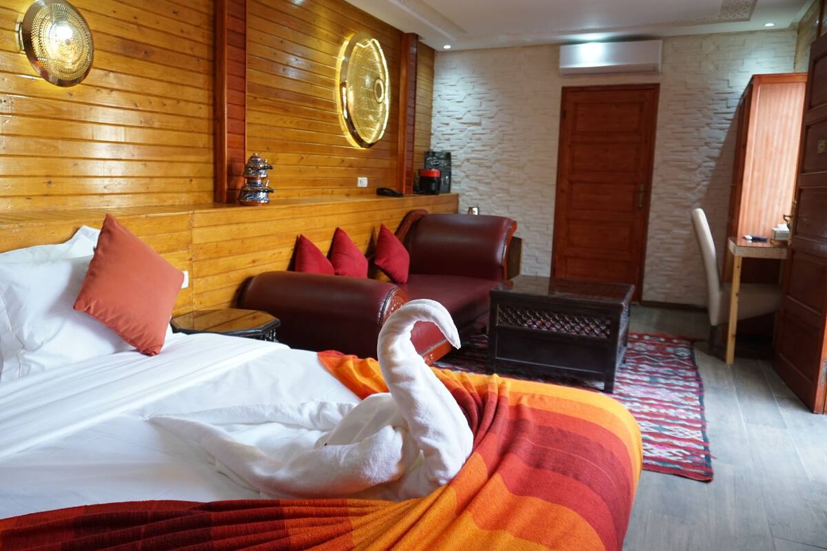 A hotel room with a bed, a wooden headboard, a desk, a chair, and a wardrobe.