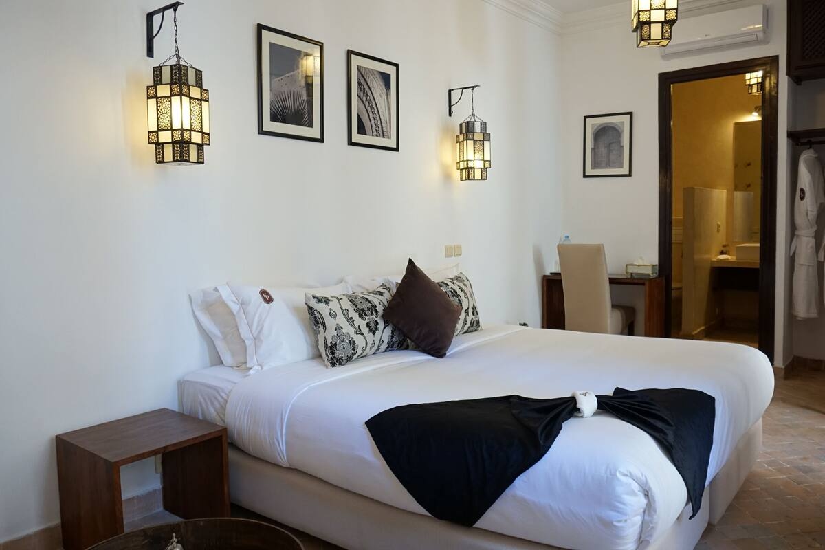 A neatly made bed with pillows, a bedside table, and wall-mounted lights.