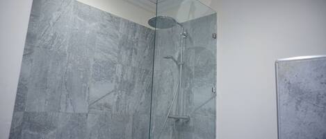 A shower with a glass door, a handheld showerhead, and a wall-mounted faucet.