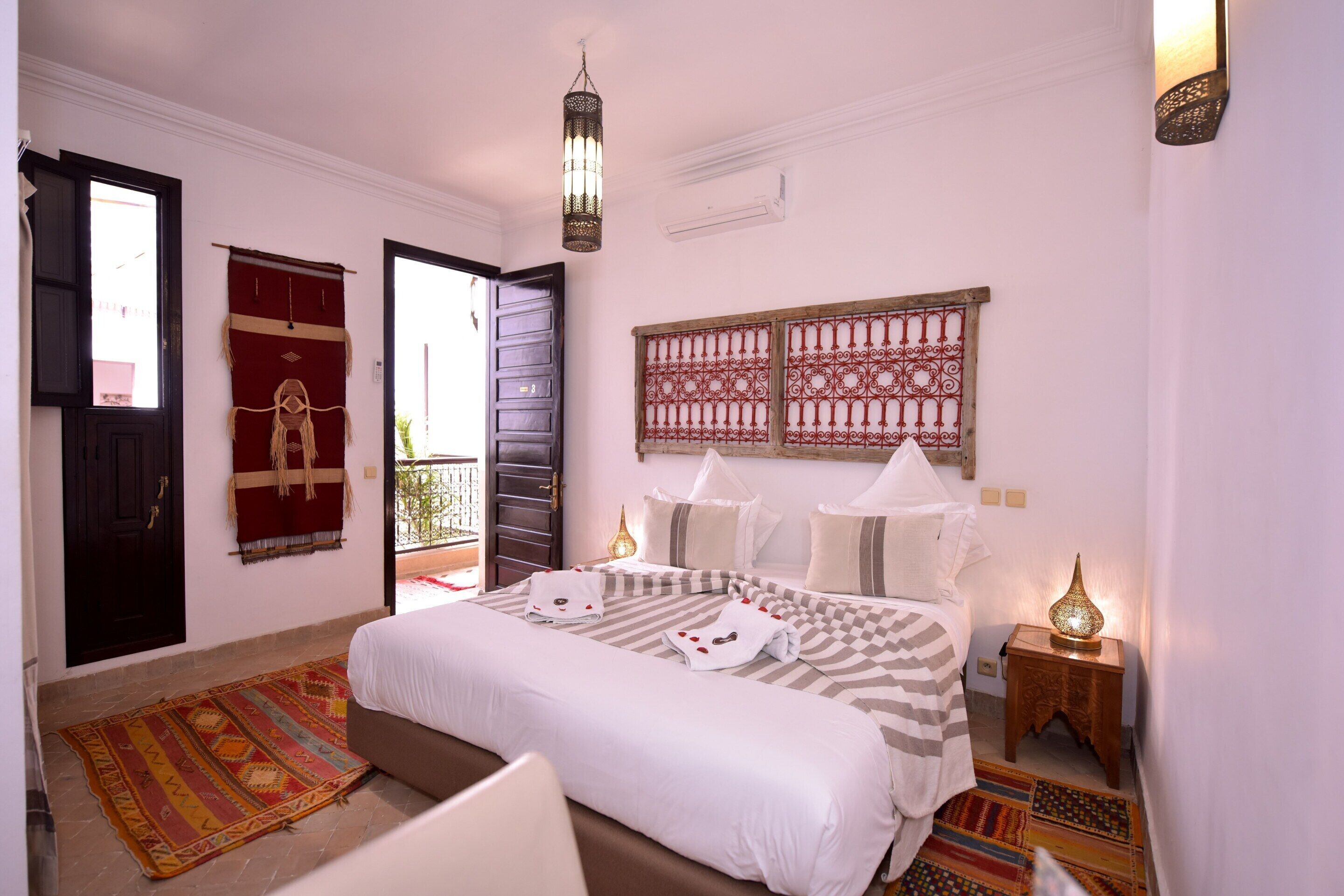 A bedroom with a bed, a nightstand, a wall-mounted lamp, a door, and a window.