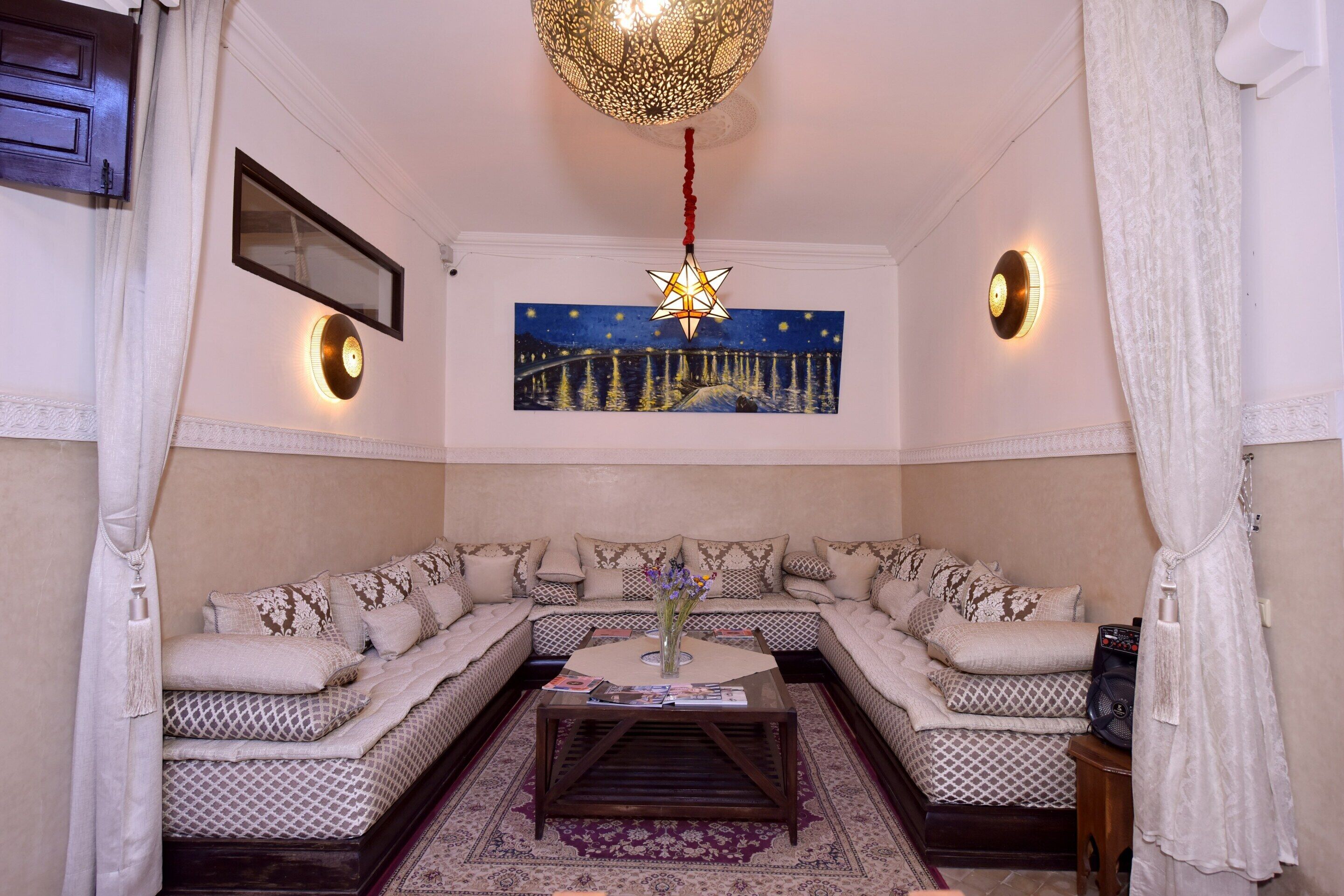 A living room with a sectional sofa, a coffee table, a wall-mounted star lantern, and a painting of a night scene.