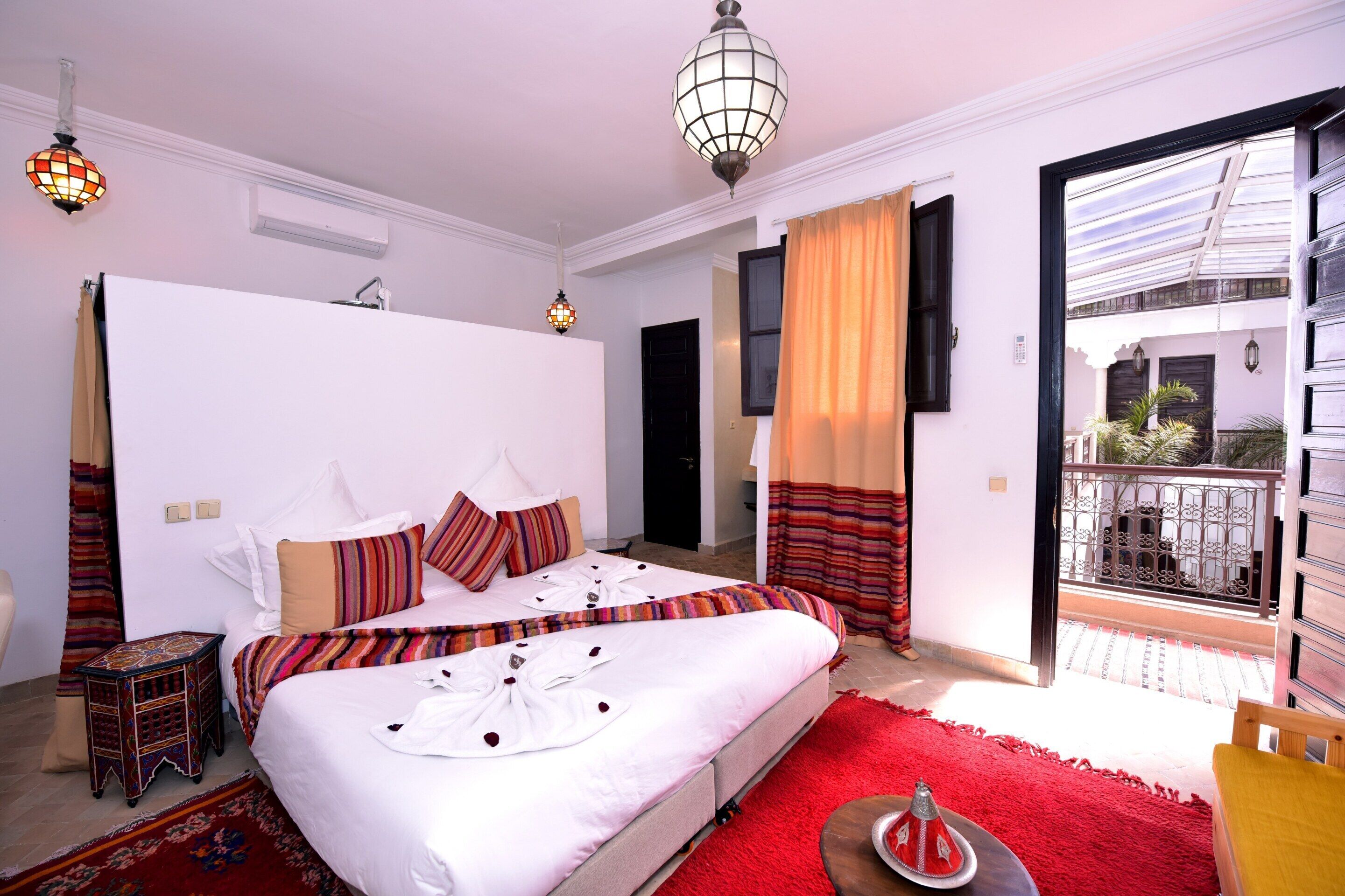 A bedroom with a large bed, a small side table, a red rug, and a balcony with a metal railing.
