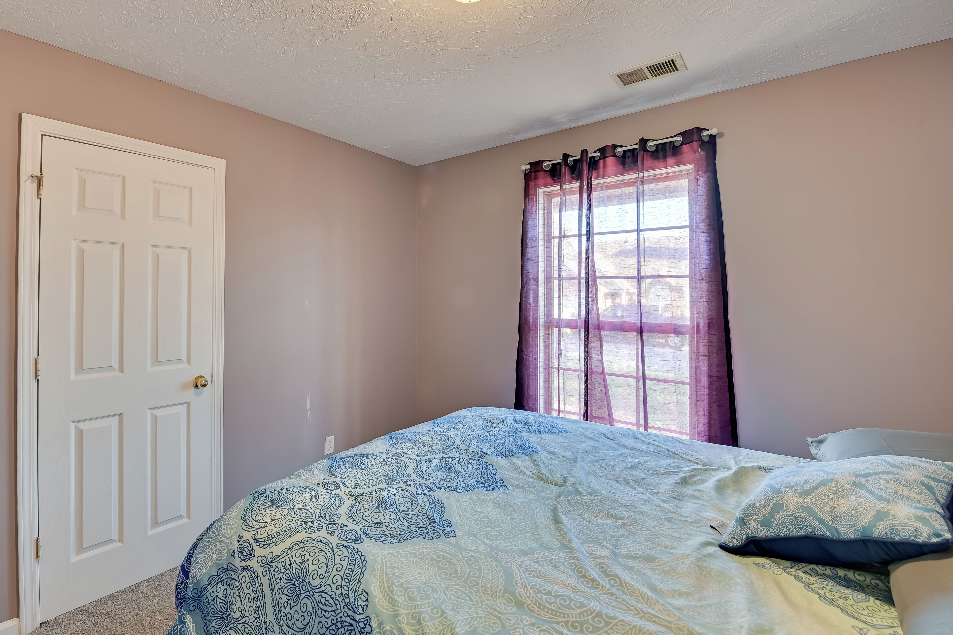 Un dormitorio con cama, puerta y ventana con cortinas.