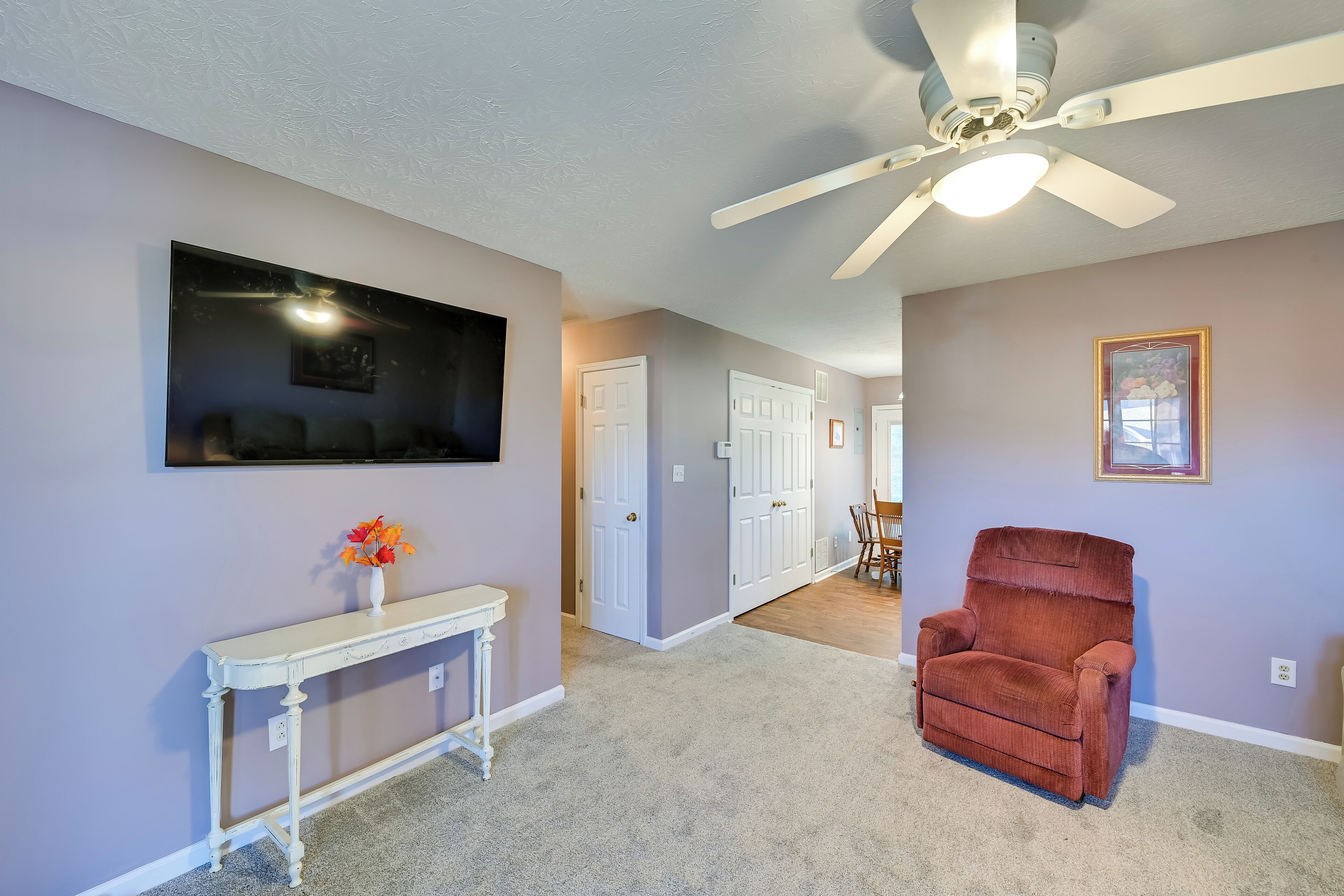 A hallway with a ceiling fan, a white console table with a vase of flowers, and a red armchair.