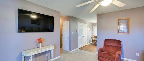 A hallway with a ceiling fan, a white console table with a vase of flowers, and a red armchair.