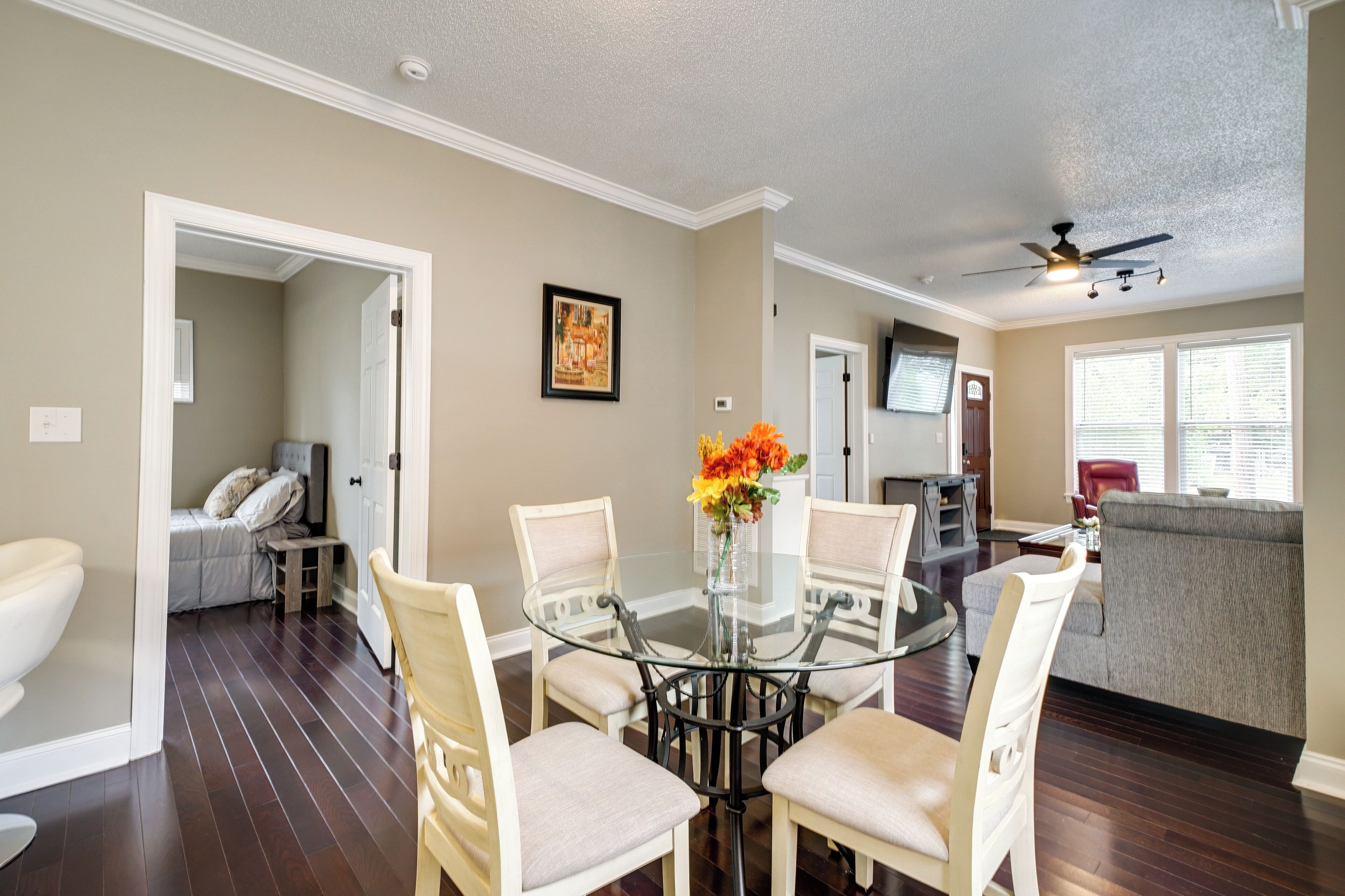 A dining area with a glass table surrounded by four chairs, a vase with flowers, and a painting on the wall.