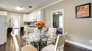A modern kitchen with white cabinets, a glass dining table, and a vase with flowers. - Downtown Wilmington Home: Walk to Cape Fear River! (Wilmington)