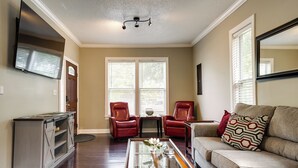 A living room with a sofa, two red chairs, a coffee table, and a TV mounted on the wall. - Downtown Wilmington Home: Walk to Cape Fear River! (Wilmington)