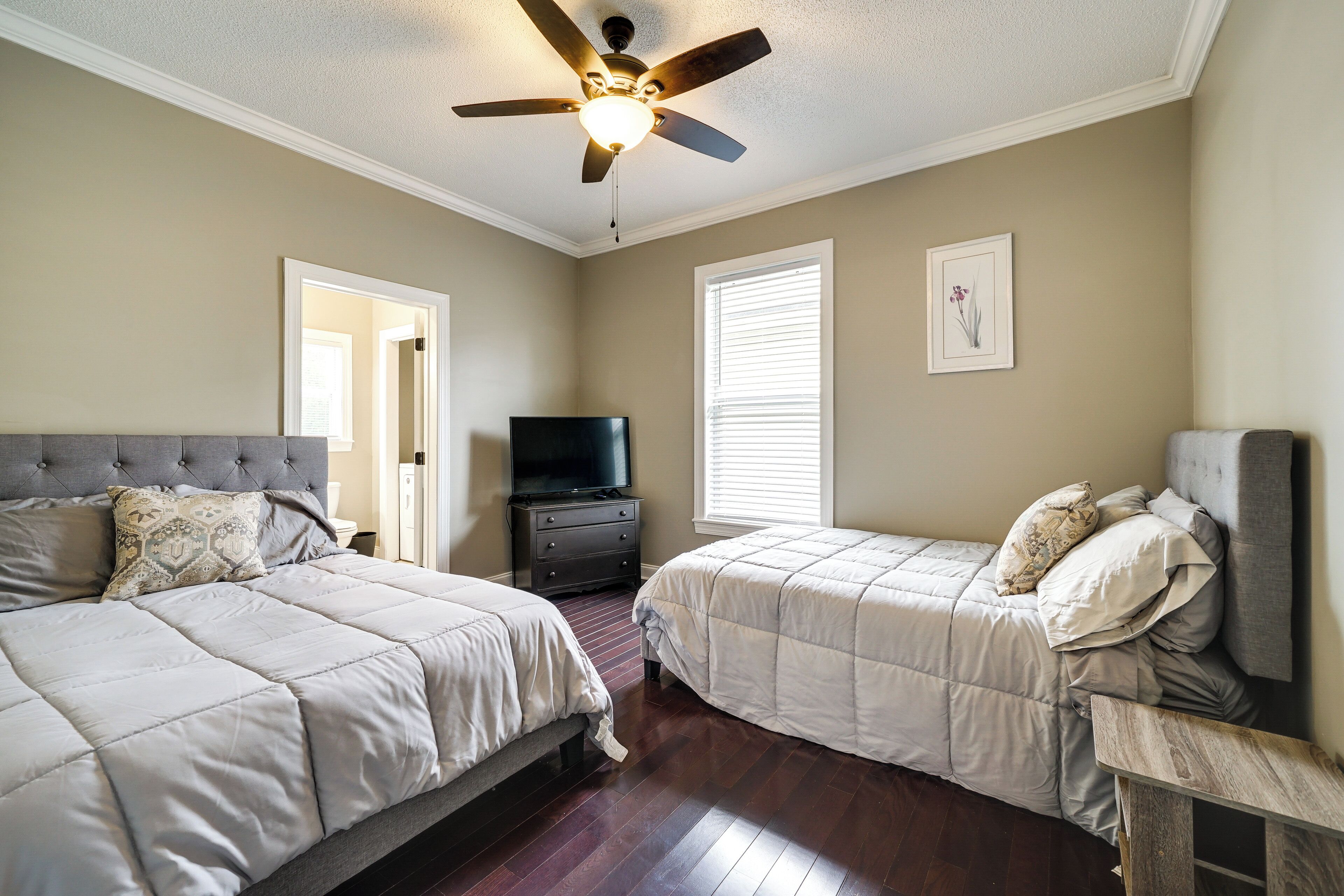 A bedroom with two beds, a ceiling fan, a TV, and a window with blinds.