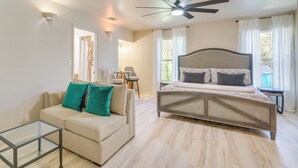 A bedroom with a bed, a sofa, a glass coffee table, and a ceiling fan.