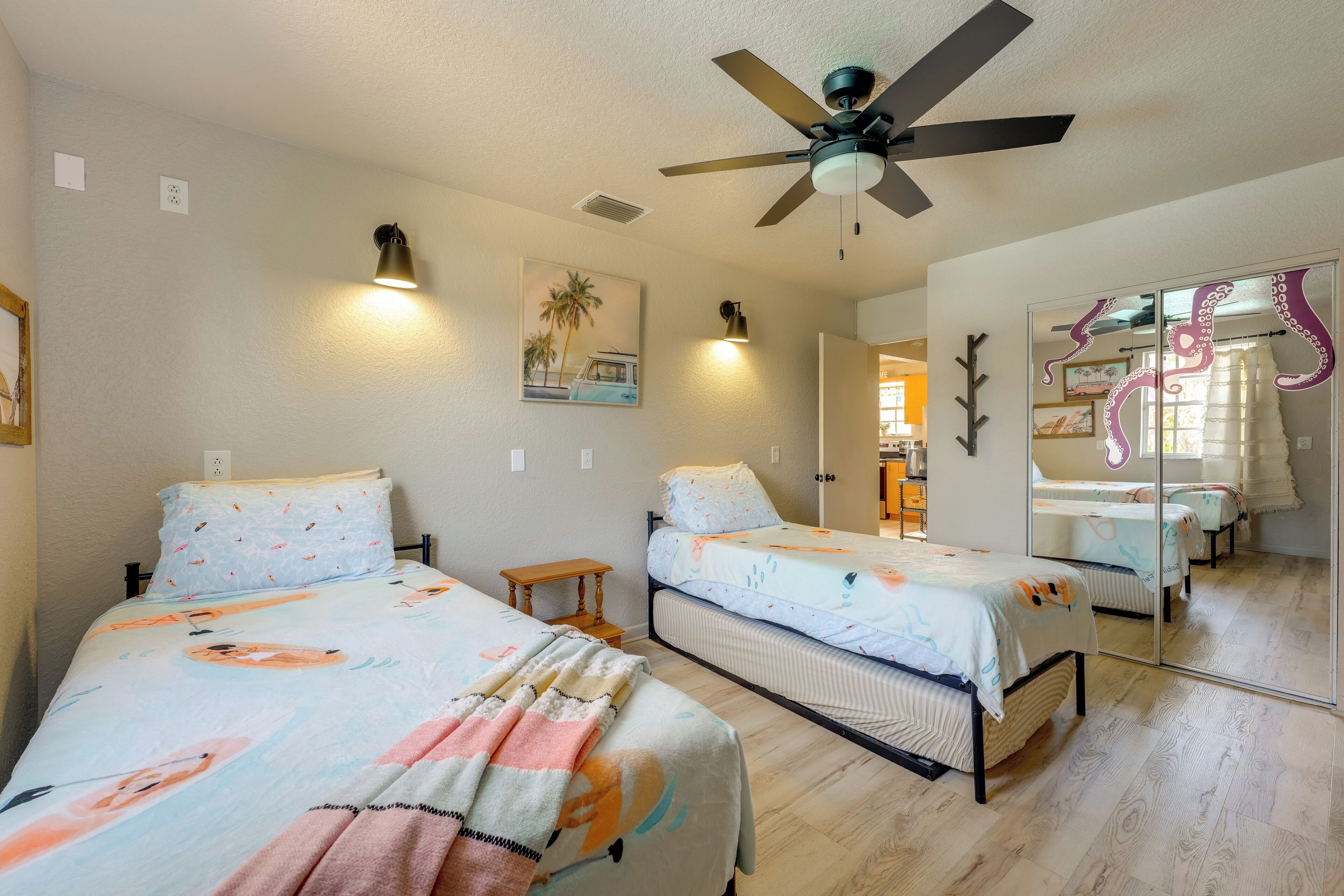A bedroom with two beds, a ceiling fan, wall-mounted lamps, and a painting.