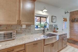 Una cocina con armarios de madera, pileta de acero inoxidable, encimeras de granito y un tostador integrado.