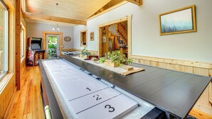 Ett biljardbord i ett rum med trägolv och träpanel på väggarna, en takfläkt och en inramad tavla på väggen.