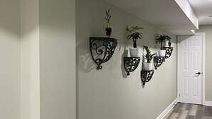 Un couloir aux murs vert clair, au plancher en bois foncé et agrémenté d’appliques murales décoratives où sont disposées des plantes.