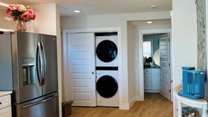 Eine moderne Küche mit einem Edelstahl-Kühlschrank, einer Waschmaschine und einem Essbereich mit einem weißen Tisch und blauen Stühlen.