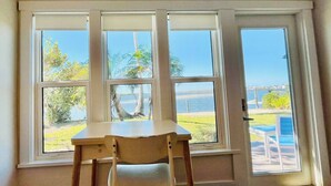 Ein Zimmer mit Holzschreibtisch und Stuhl, große Fenster mit Blick auf Strand und Palmen.