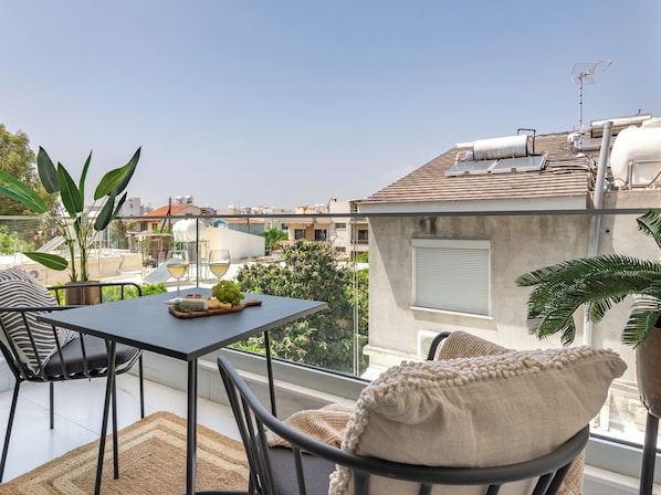 A balcony with a table set for two, a chair, and a potted plant. - Sanders Cruise - Lovely Studio Apt With Balcony (Limassol)