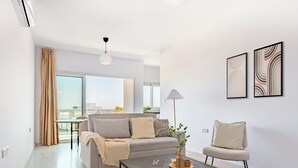 Ein modernes Wohnzimmer mit einer Couch, Couchtisch und Sessel, großen Fenstern und abstrakter Wandkunst.